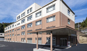介護施設の建物外観。白とベージュの外壁、複数階建て、玄関入口が見える。
